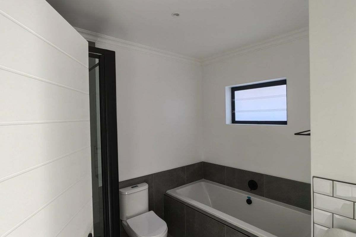 Modern bathroom featuring a built-in bathtub with dark grey tiling, a white toilet, and a small window with black framing.