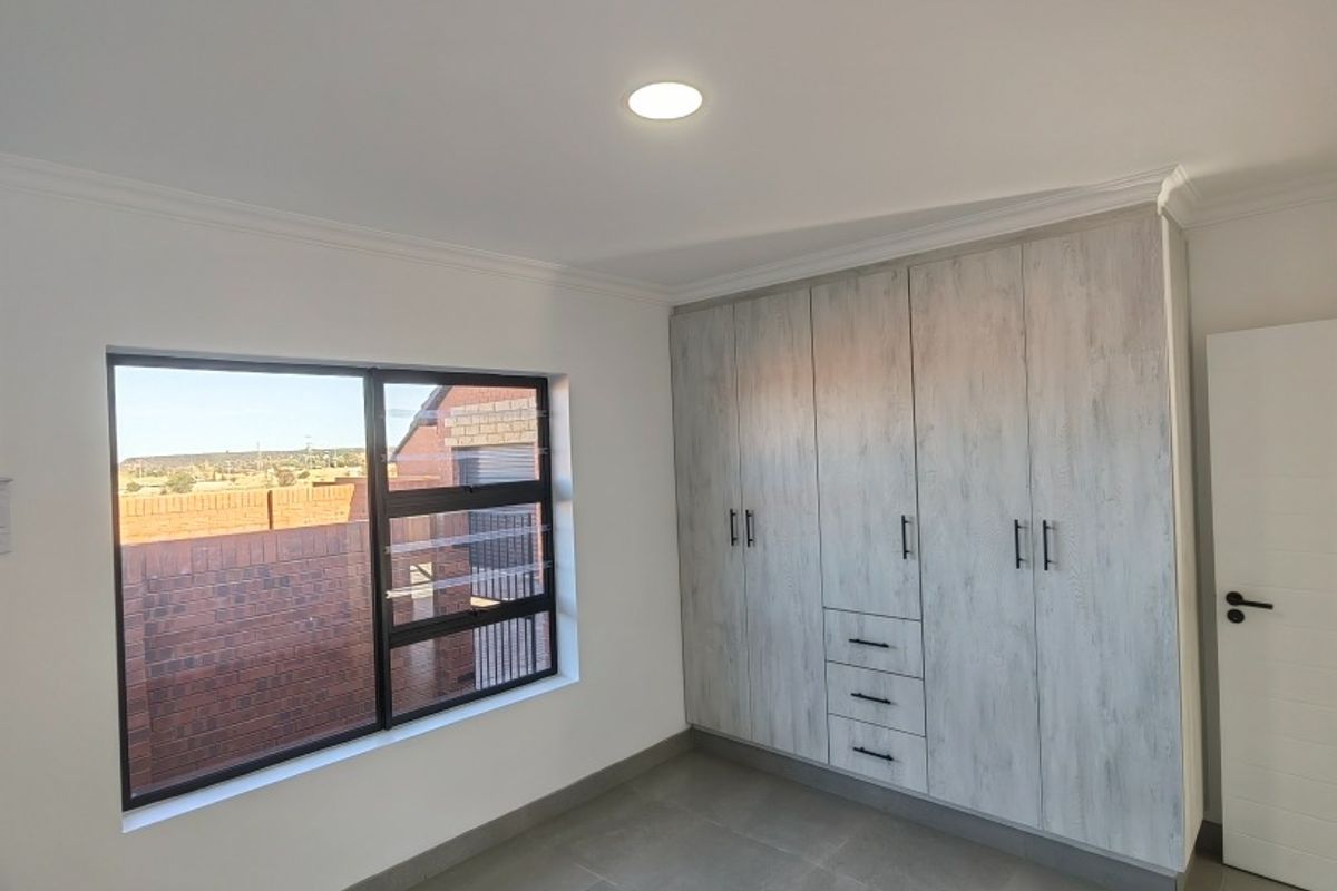 A bright, modern bedroom featuring neutral floor tiles, recessed ceiling lighting, and extensive built-in cabinetry with a contemporary wood-grain finish.