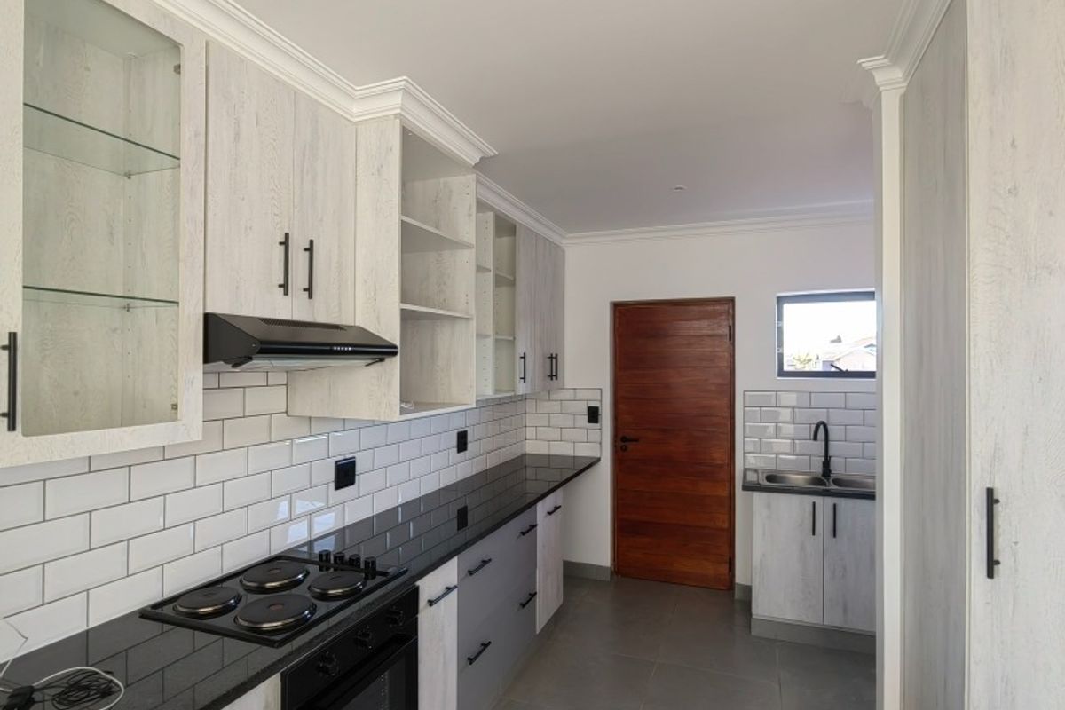 Modern kitchen featuring light wood-grain cabinetry, black granite countertops, subway tile backsplash, built-in oven, hob, extractor fan, and a double sink.