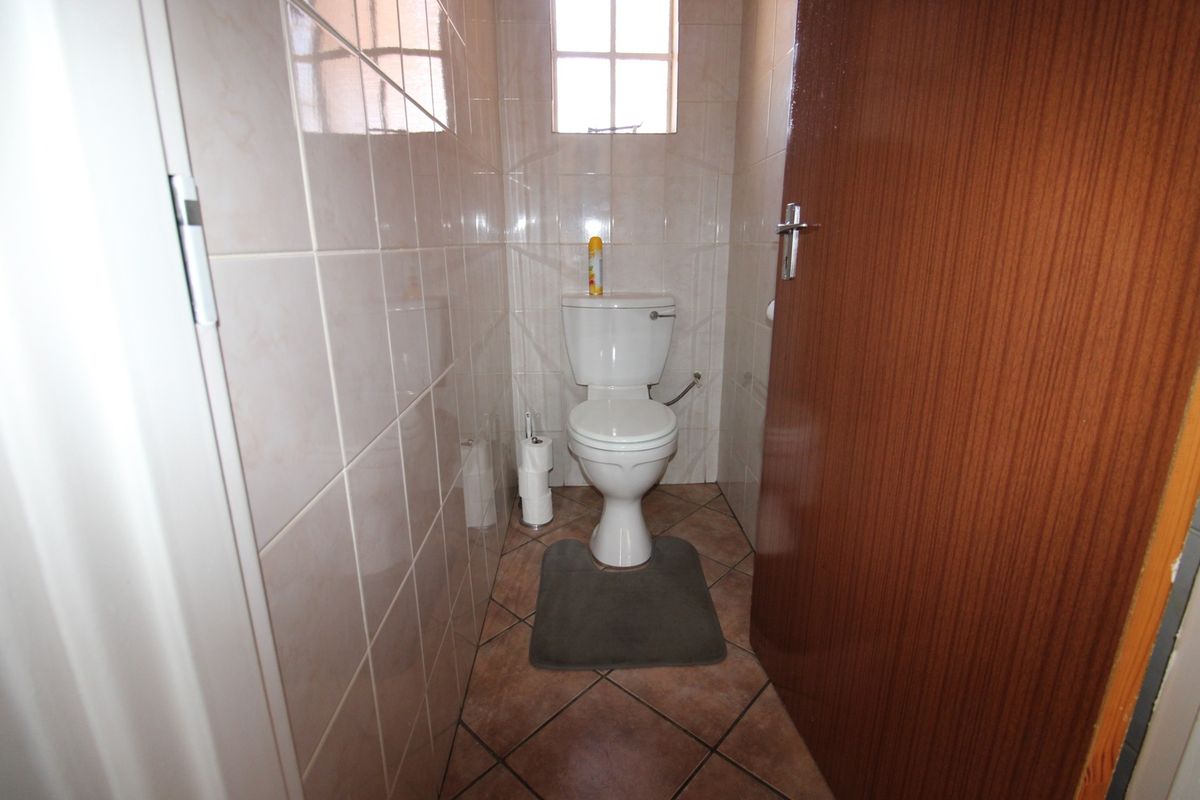 A compact guest toilet featuring floor-to-ceiling wall tiles, tiled flooring, and a standard white ceramic toilet suite.
