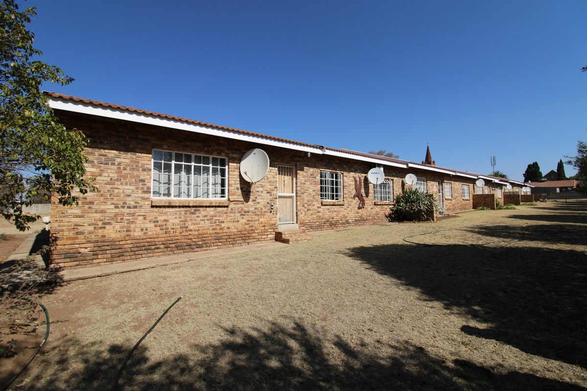 A view of the rear exterior of a brick residential building featuring multiple units, security gates, and satellite dishes set against a large lawn.
