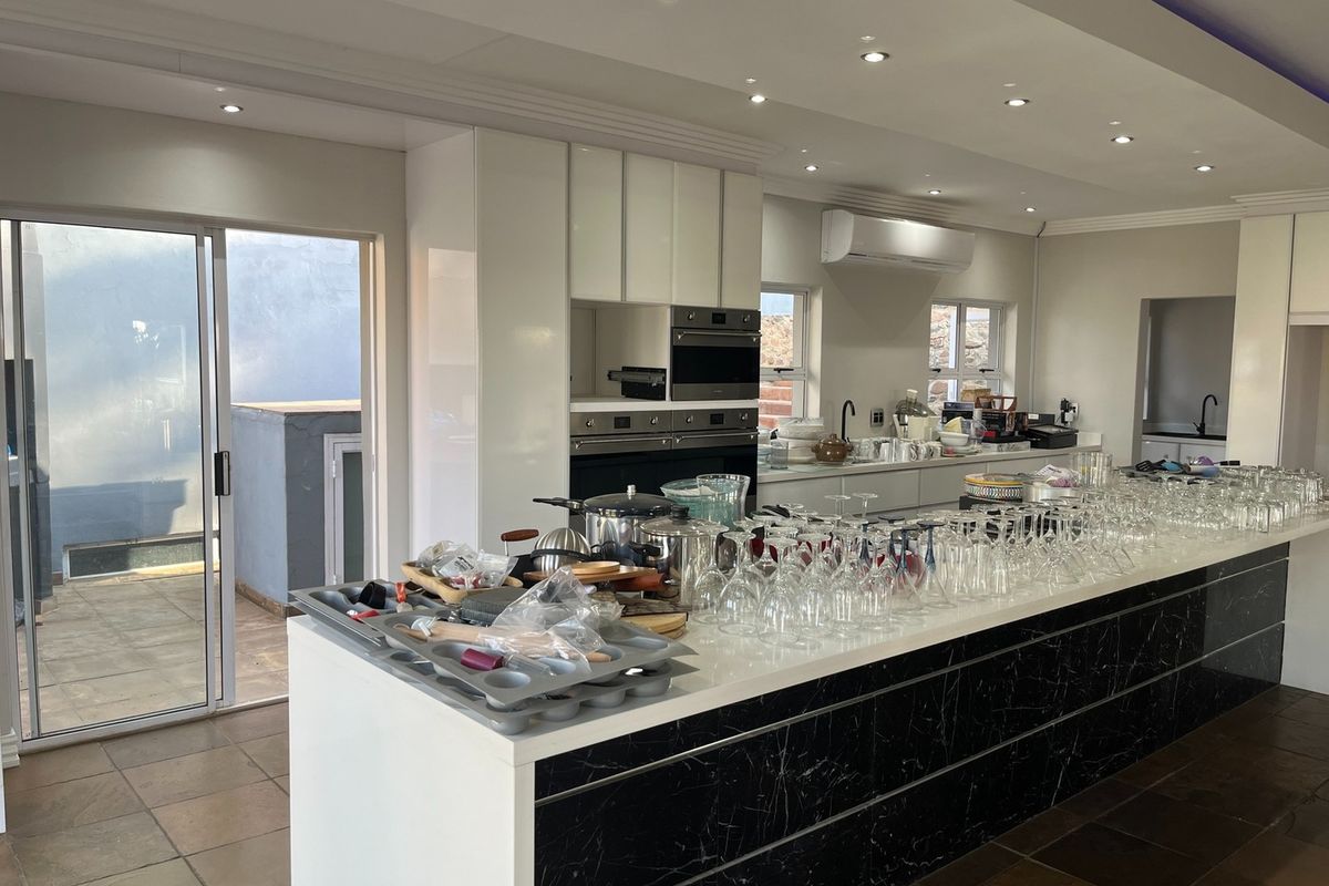 Modern open-plan kitchen featuring a large central island with marble-effect cabinetry, built-in ovens, recessed ceiling lighting, and direct access to an outdoor patio area.