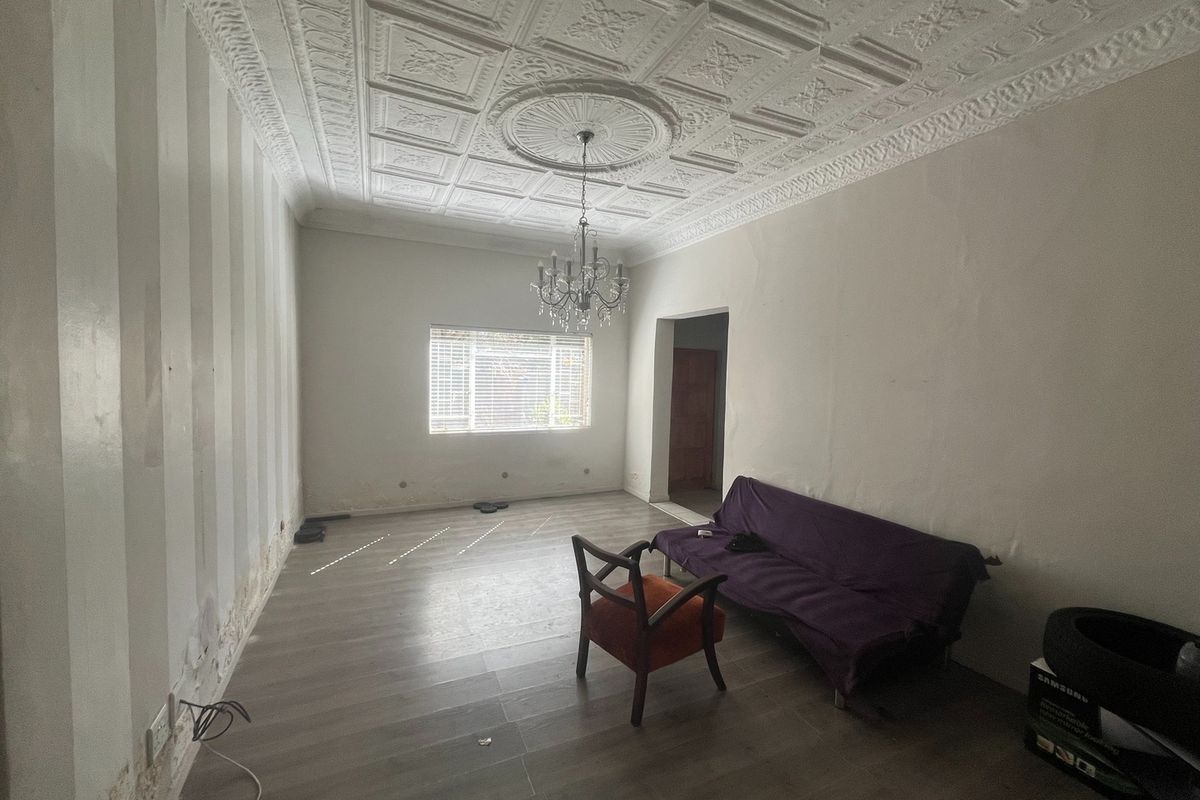 A living room featuring a decorative pressed metal ceiling, chandelier, and wood-look flooring, requiring cosmetic wall repairs.