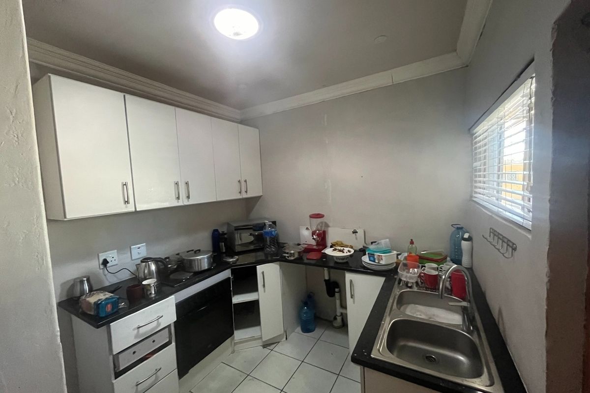 A functional kitchen featuring white cabinetry, black countertops, a double stainless steel sink, and tiled flooring.