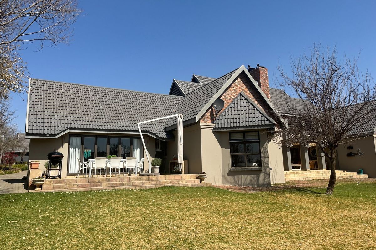 Rear view of the house featuring a tiled roof, brick chimney, paved patio area, and a well-maintained garden.
