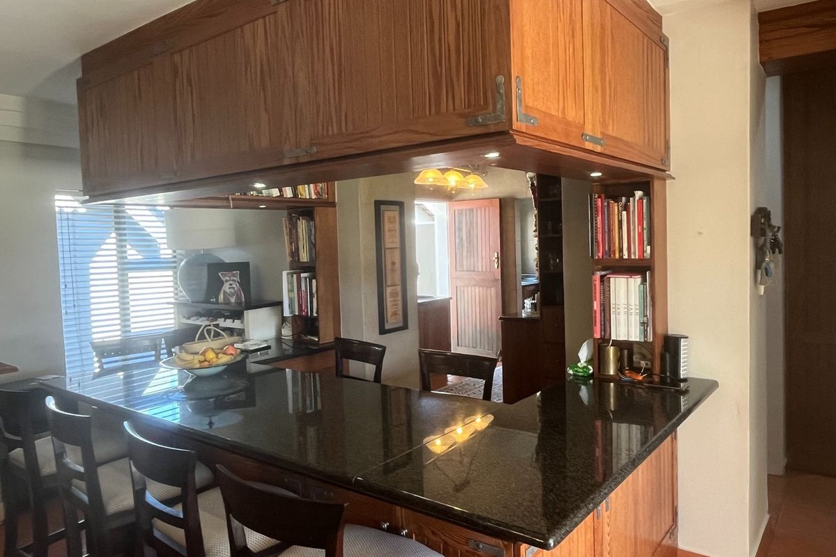 A kitchen area featuring a dark granite breakfast bar, wooden cabinetry, and integrated shelving, providing a functional and classic layout.