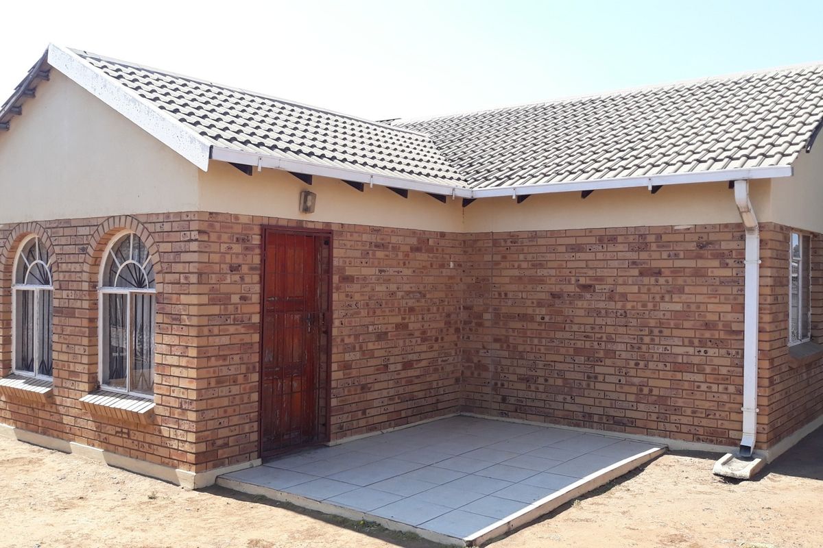 Exterior view of a face brick house featuring a tiled roof, arched windows with security bars, and a small tiled patio area.