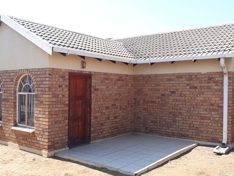 Exterior view of a face brick house featuring a tiled roof, arched windows with security bars, and a small tiled patio area.