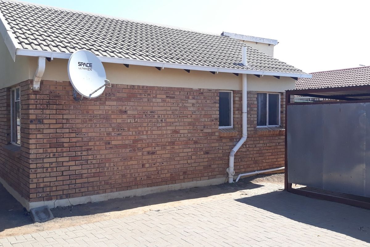 Rear exterior view of a face brick house featuring a tiled roof, paved driveway, and a metal carport structure.
