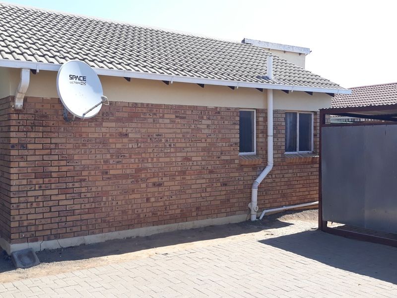Rear exterior view of a face brick house featuring a tiled roof, paved driveway, and a metal carport structure.