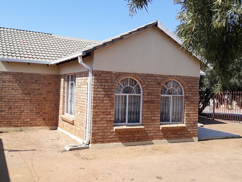 Front view of a face brick house featuring arched windows, a tiled roof, and perimeter security fencing.
