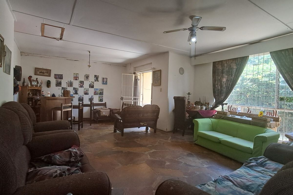 Spacious living area featuring large windows with security bars, ceiling fan, and stone-tiled flooring, offering a functional layout with direct access to the exterior.