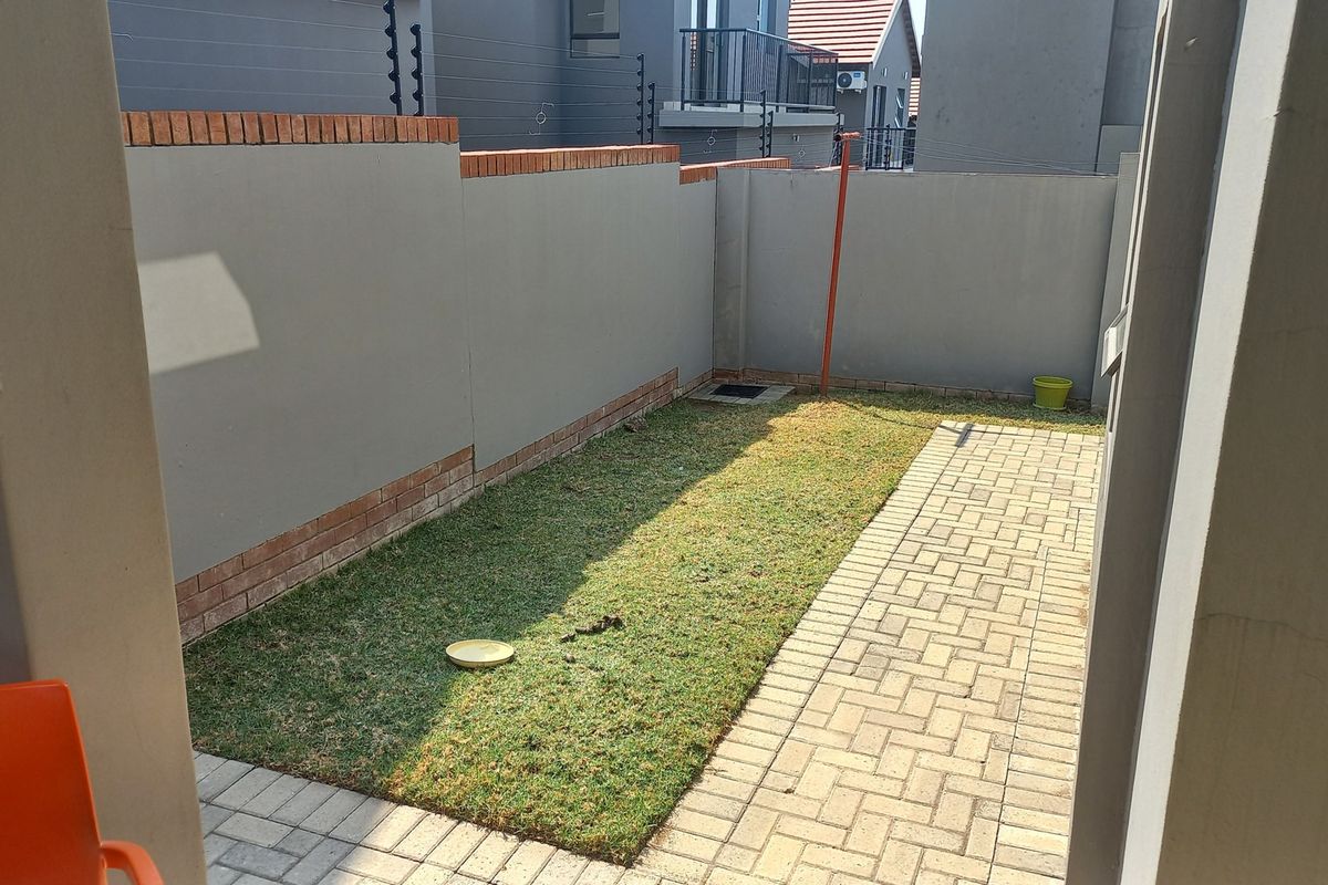 A private rear garden featuring a paved walkway, a small lawn area, and high perimeter boundary walls with brick detailing.