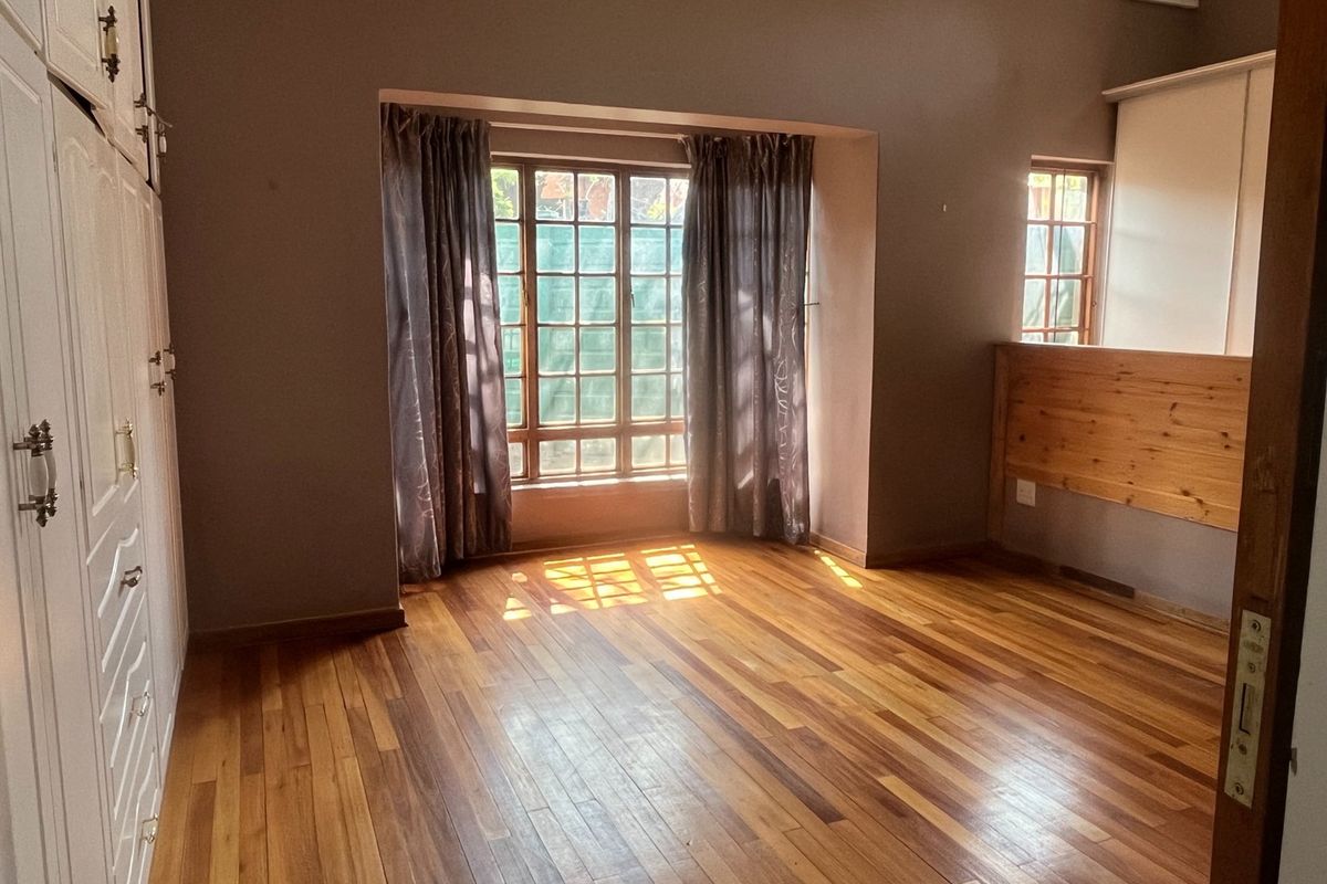 A spacious bedroom featuring polished wooden flooring, built-in cabinetry, and large windows that allow for ample natural light.