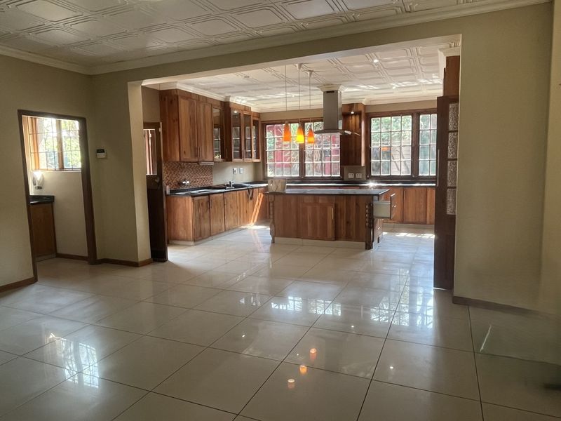 Spacious open-plan kitchen featuring timber cabinetry, a central island, tiled flooring, and a coffered ceiling, providing a functional and warm cooking environment.