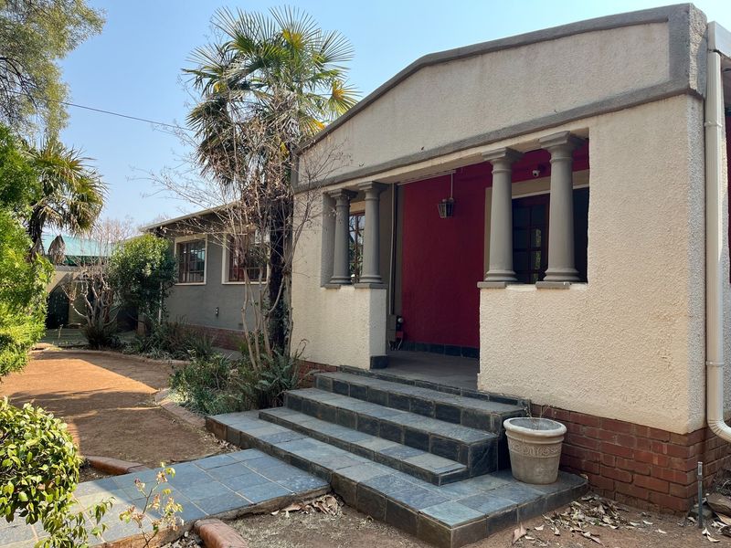 A charming exterior view of the home featuring a covered entrance porch with classical columns, stone-tiled steps, and a landscaped garden area.