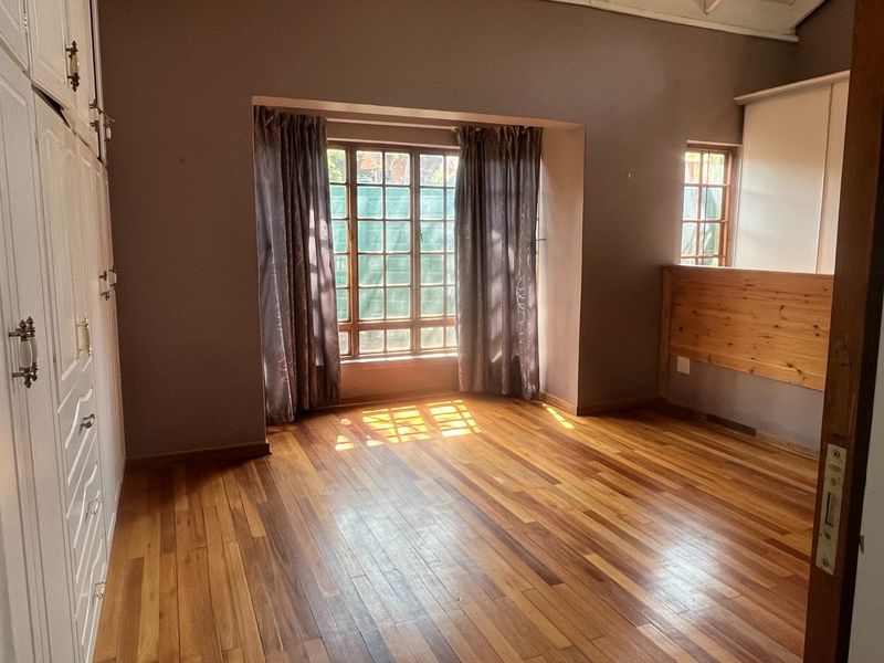 A spacious bedroom featuring polished wooden flooring, built-in cabinetry, and large windows that allow for ample natural light.