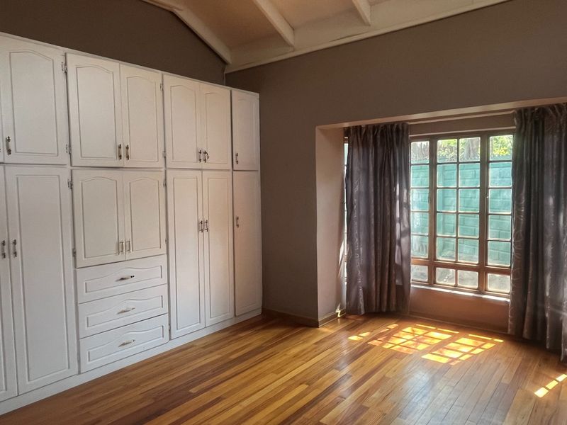 A bright bedroom featuring polished wooden flooring, vaulted ceilings, and extensive built-in white cabinetry providing ample storage space.