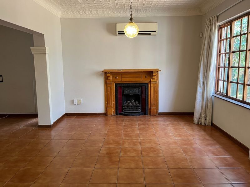 A spacious living room featuring a classic wooden fireplace mantel, tiled flooring, decorative ceiling cornice, and a wall-mounted air conditioning unit.