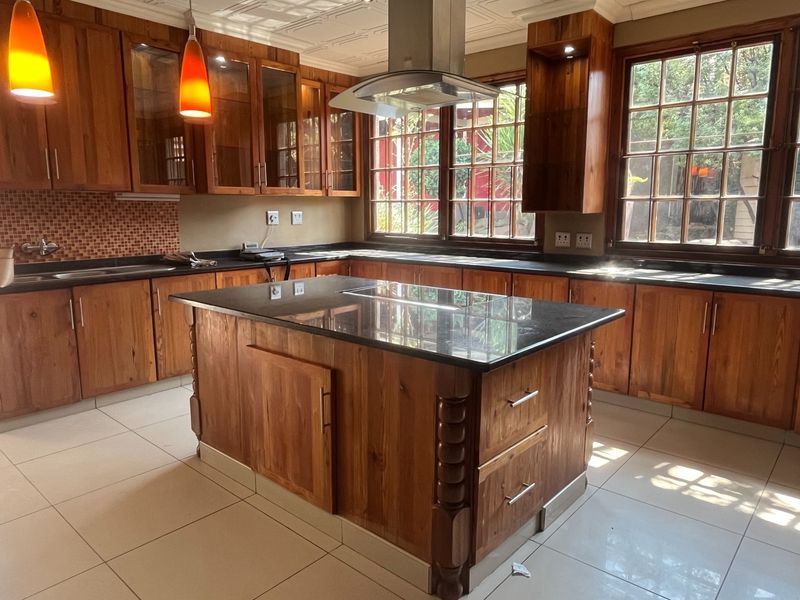 Spacious kitchen featuring solid wood cabinetry, a central island with a dark stone countertop, stainless steel extractor fan, and tiled flooring.