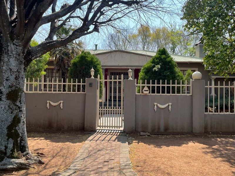Front view of a house featuring a secure gated entrance, brick paved walkway, and a perimeter wall with decorative accents.