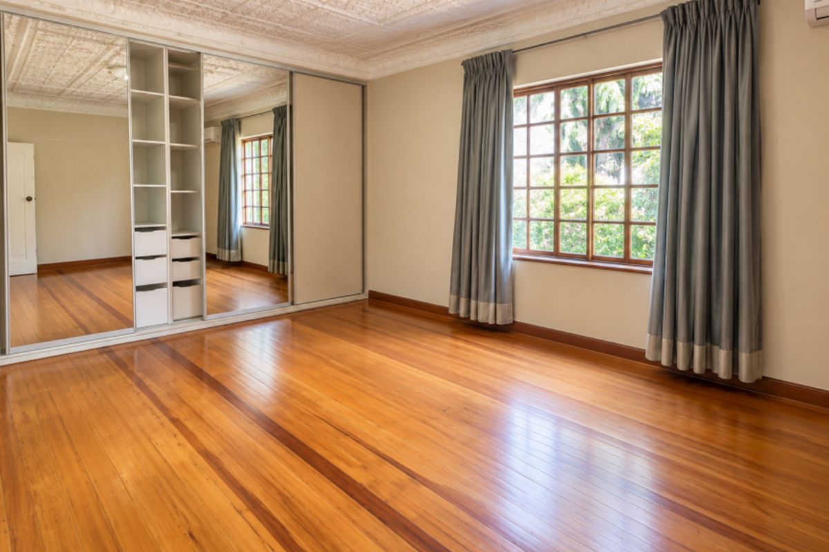 Spacious bedroom featuring polished hardwood flooring, a decorative pressed metal ceiling, and a large built-in mirrored wardrobe with integrated shelving.