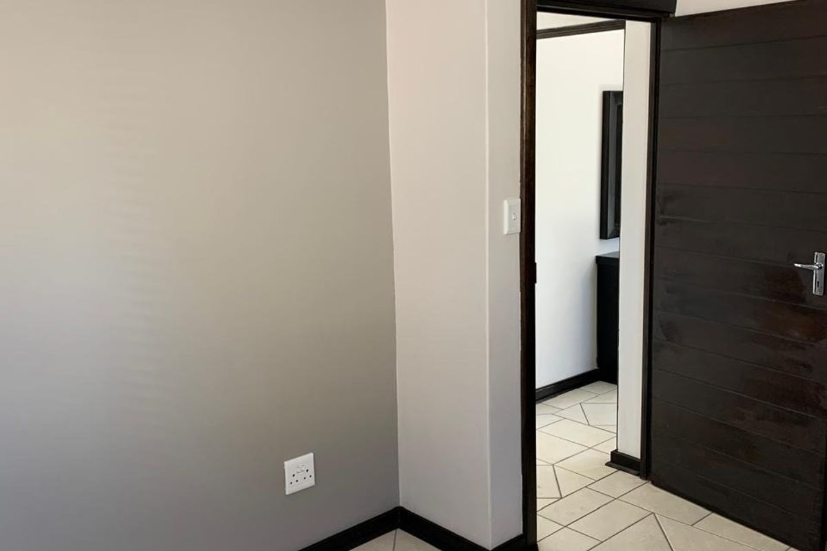 A clean, neutral-toned bedroom featuring tiled flooring, dark wood door, and a doorway leading to an adjacent room.