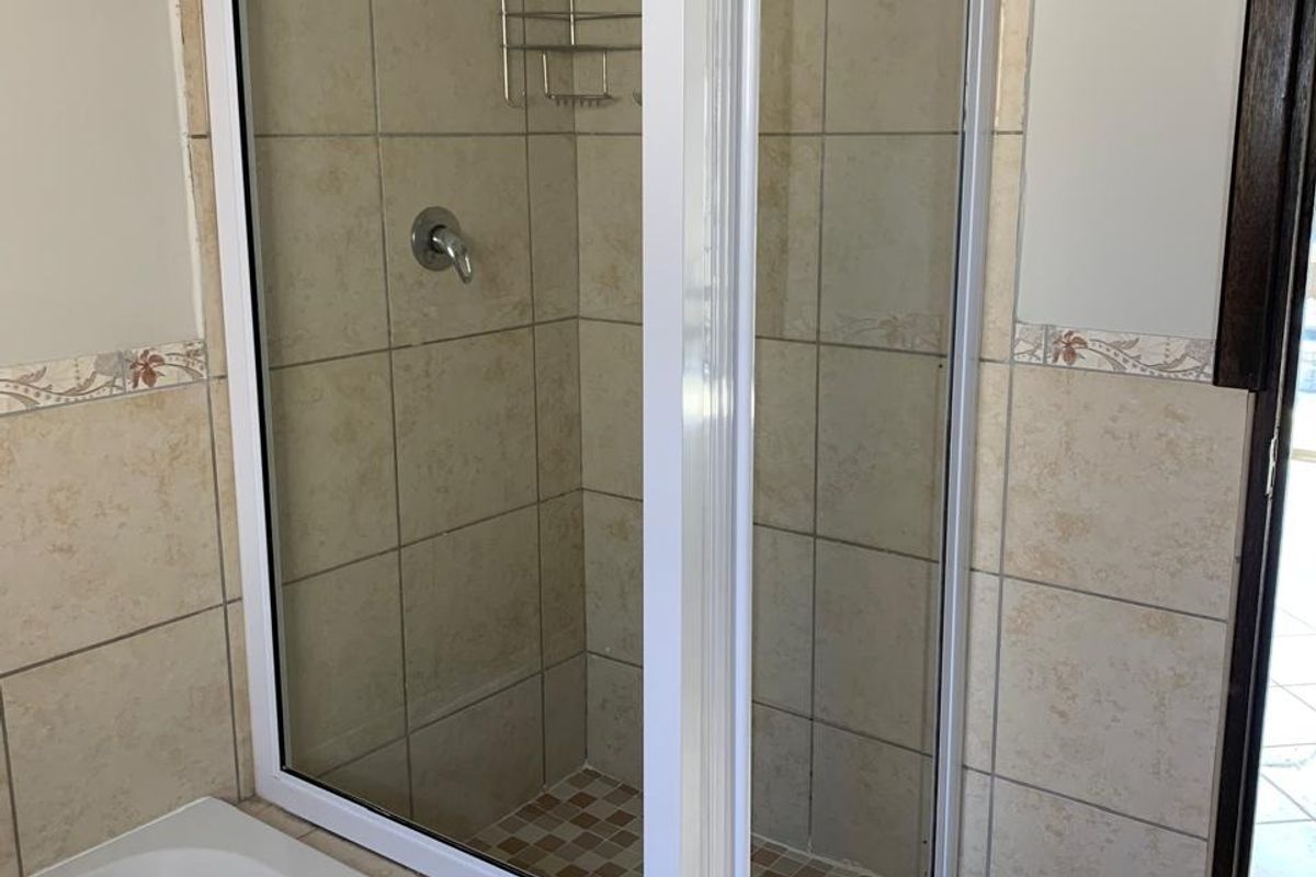 A functional bathroom featuring a corner shower enclosure with white framing, tiled walls, and a built-in bathtub.