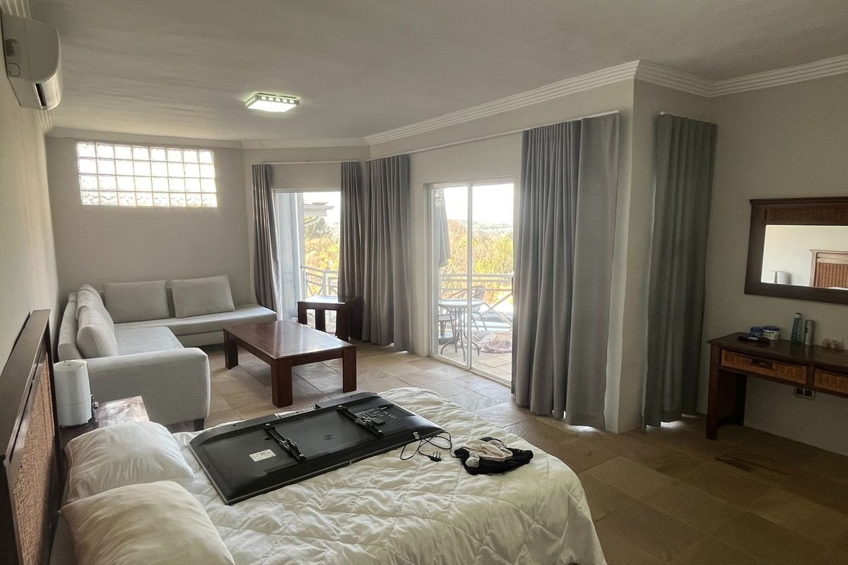 Spacious bedroom featuring tiled flooring, glass block window, wall-mounted air conditioning unit, and sliding glass doors leading to an outdoor balcony area.