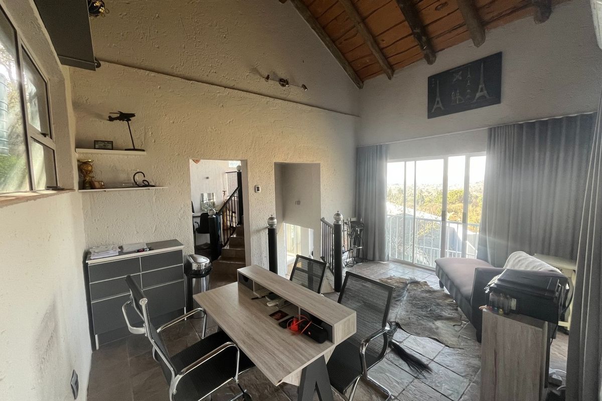 Spacious living area featuring high vaulted timber-beamed ceilings, tiled flooring, and large sliding glass doors opening to a balcony with scenic views.