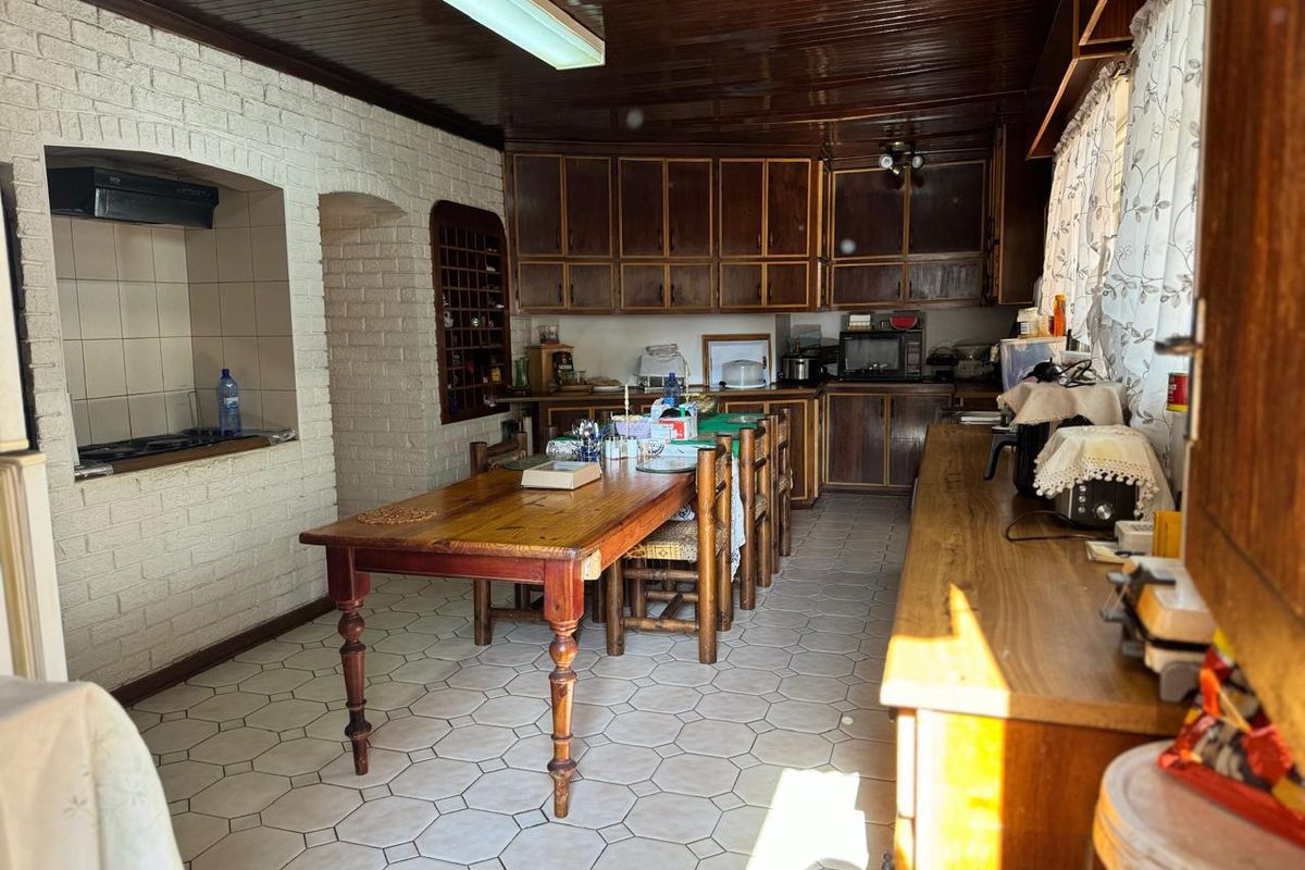 A dated kitchen featuring dark wood cabinetry, a built-in stove nook with brick surround, and a timber-paneled ceiling.