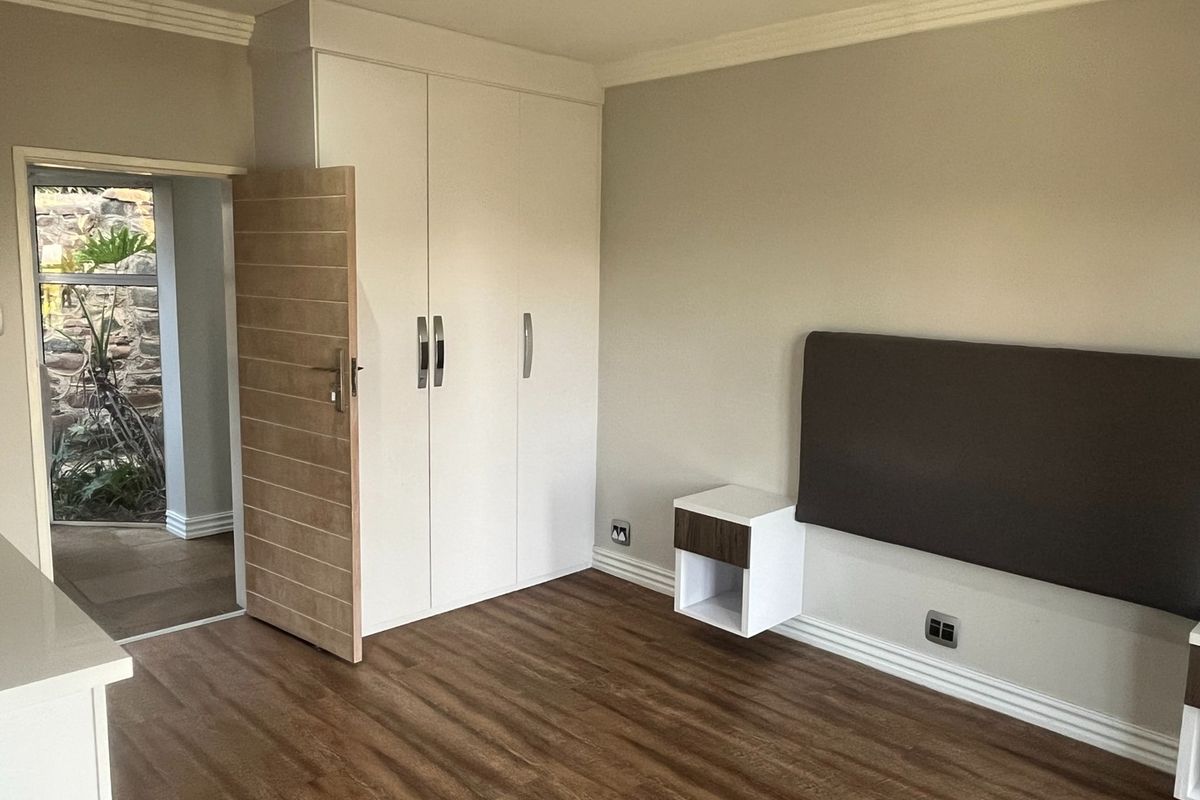 A well-maintained bedroom featuring built-in wardrobes, a floating bedside table, and a wall-mounted headboard, with wood-look flooring and crown molding.
