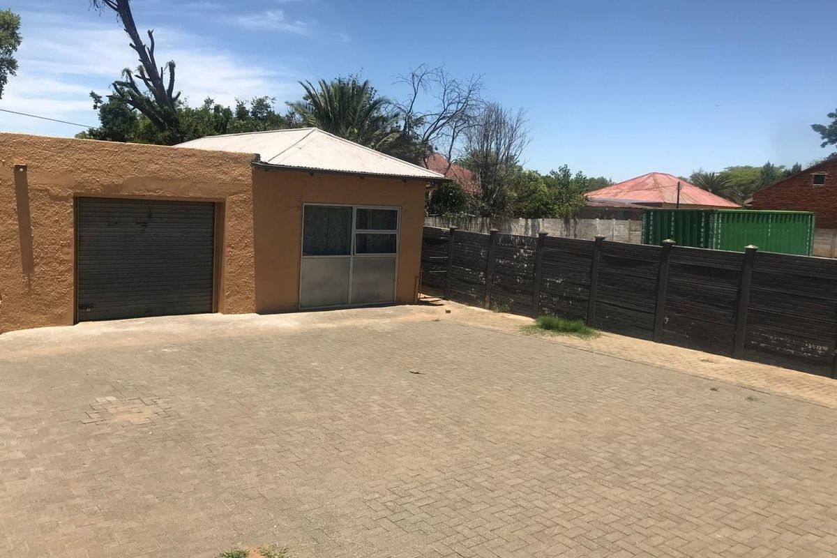 Rear exterior view featuring a detached garage, paved driveway area, and perimeter timber fencing.
