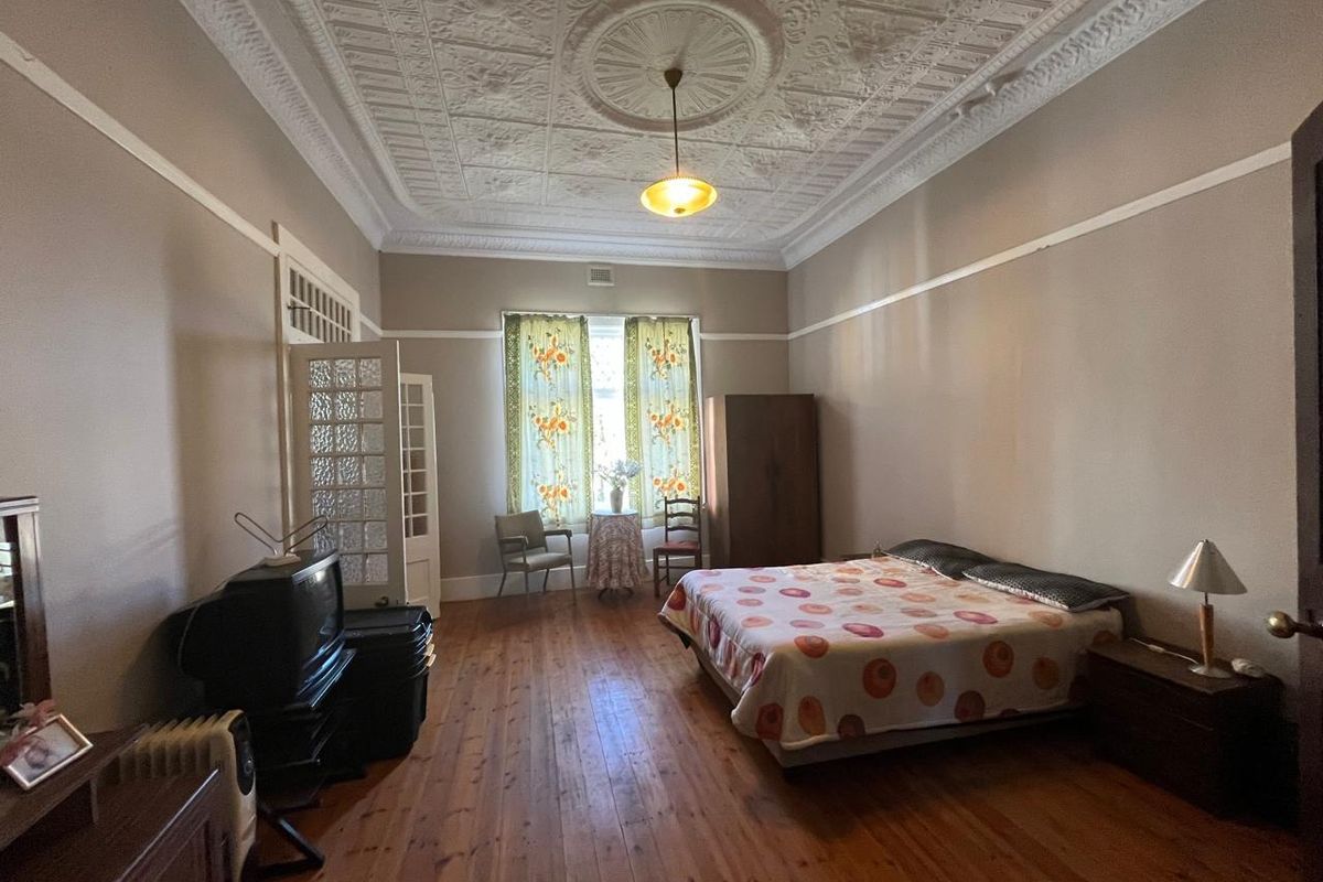 Spacious bedroom featuring original timber floorboards, high ceilings with ornate pressed metal detailing, and classic picture rails.