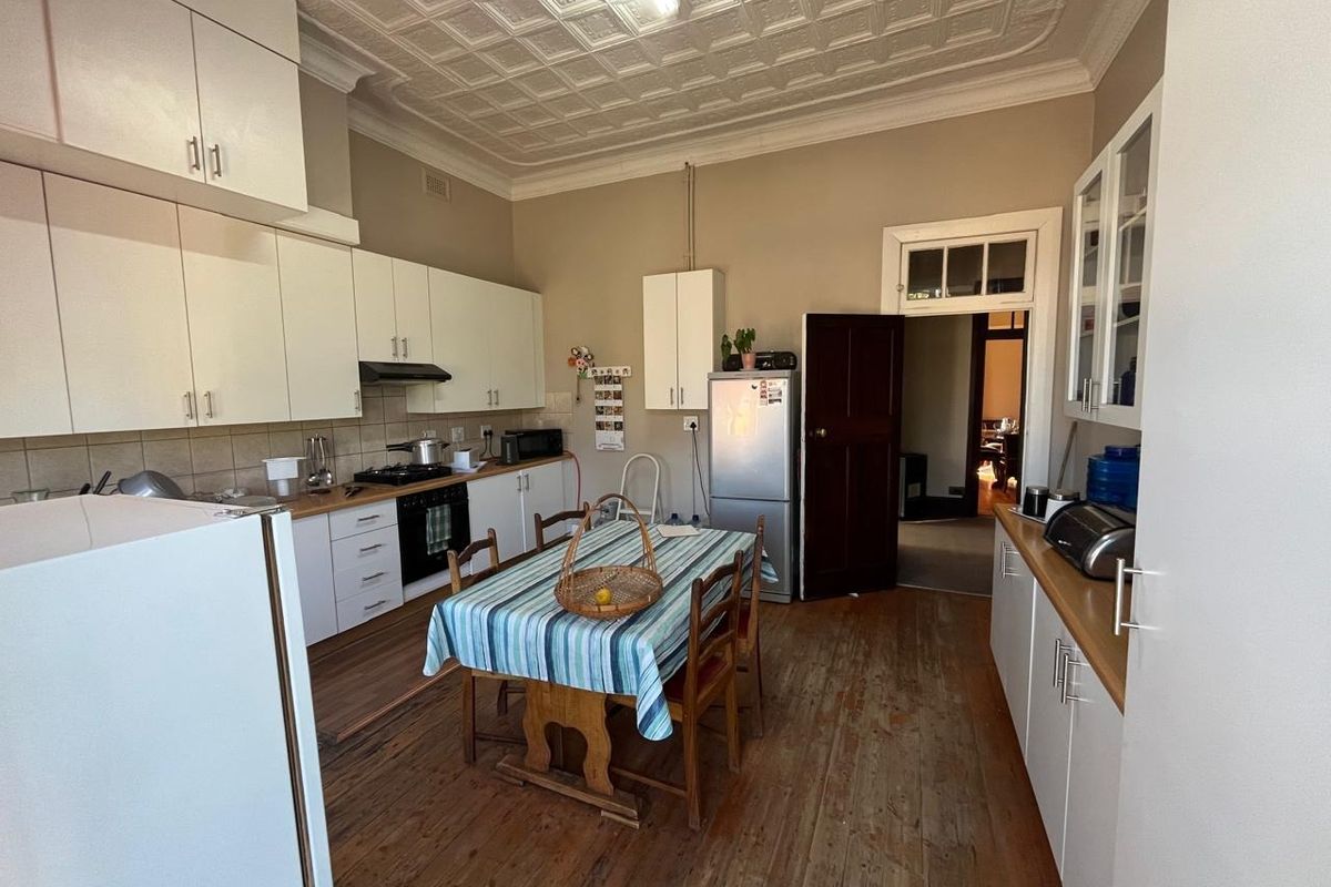 A functional kitchen featuring white cabinetry, timber flooring, and a classic pressed metal ceiling, offering a traditional aesthetic with potential for modern updates.