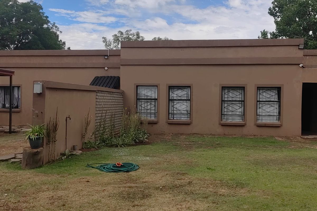 A rear view of the property featuring a flat-roofed exterior facade with security bars on windows and an adjacent lawn area.