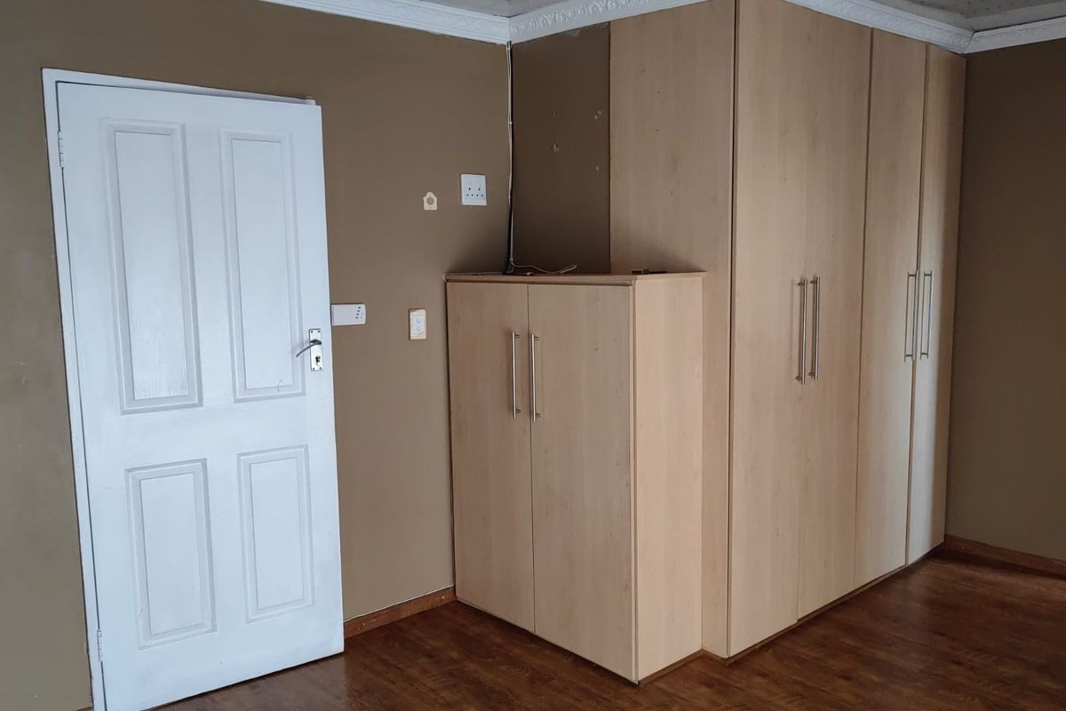 A bedroom featuring built-in light wood cabinetry, laminate flooring, and decorative ceiling cornicing.