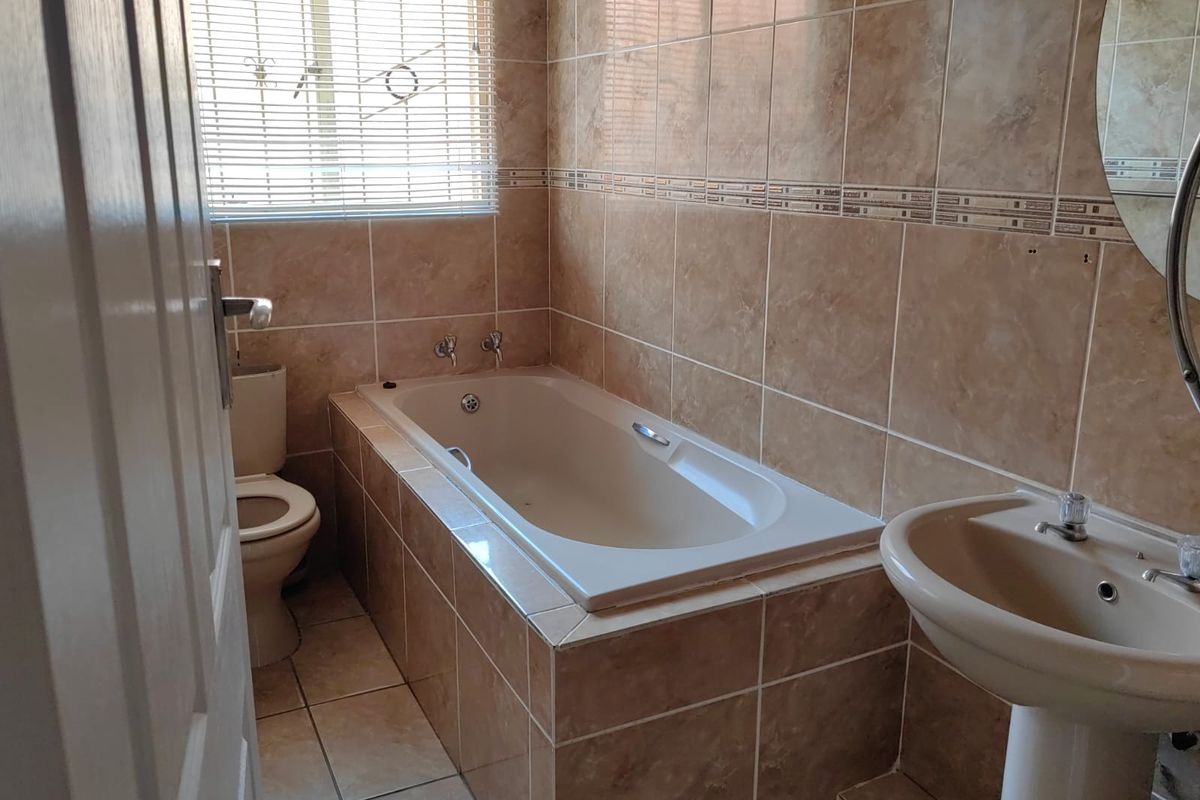 A functional bathroom featuring a built-in bathtub, pedestal basin, and toilet, finished with neutral wall and floor tiling.