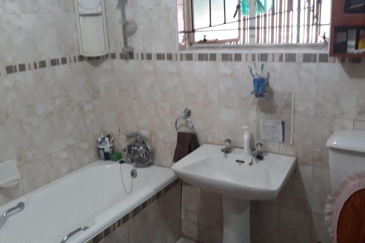 A functional bathroom featuring a pedestal sink, bathtub with shower mixer, and tiled walls with decorative border accents.