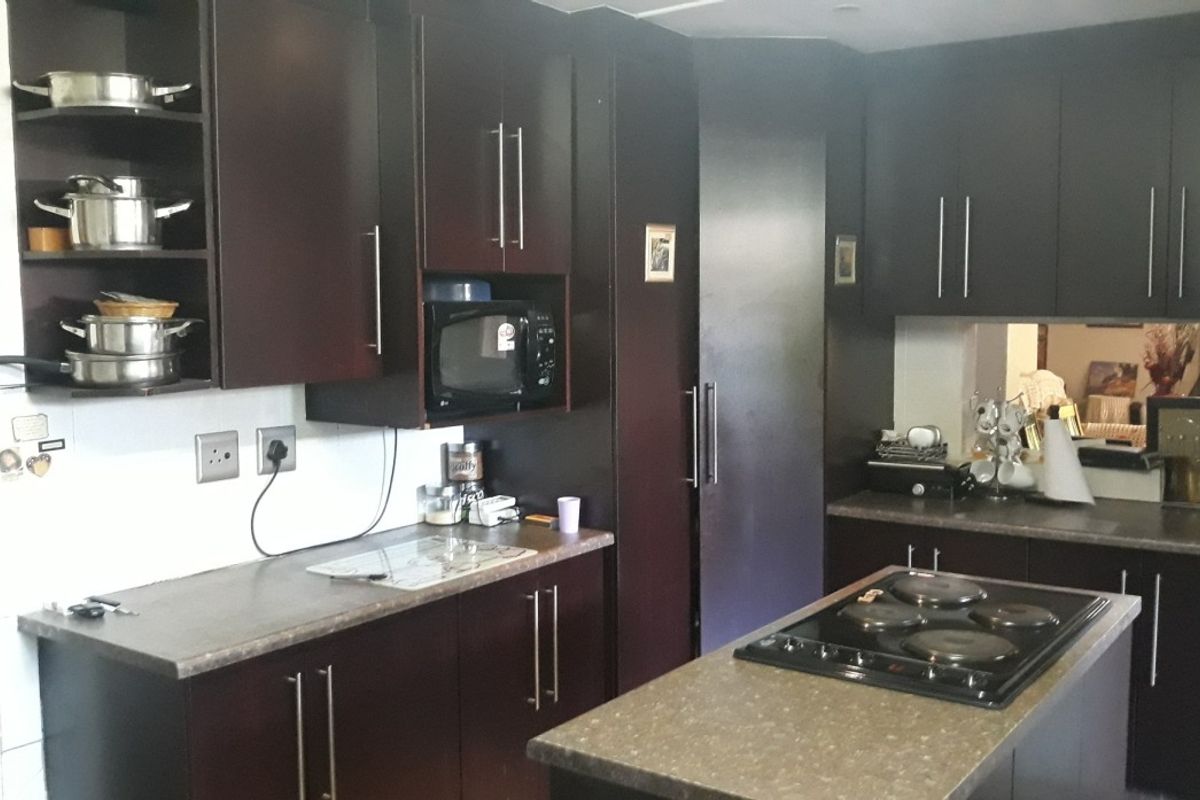 A functional kitchen featuring dark cabinetry, stone-look countertops, and a central island with a built-in electric hob.