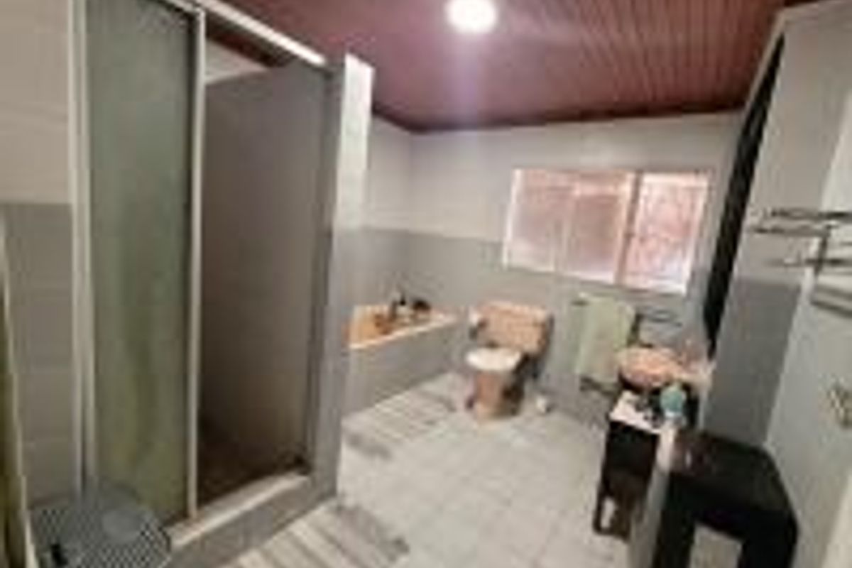 A dated bathroom featuring a shower enclosure, built-in bathtub, toilet, and vanity basin with tiled flooring and a timber ceiling.
