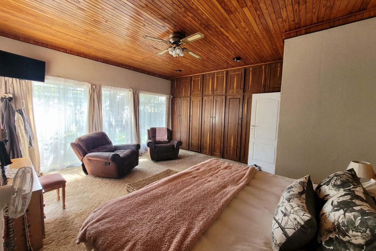 Spacious bedroom featuring a warm timber-clad ceiling, extensive built-in cabinetry, and large windows allowing for ample natural light.