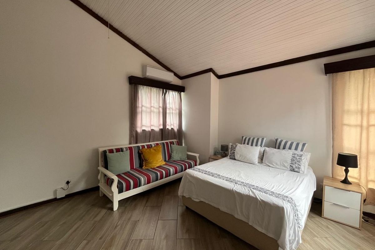 A spacious bedroom featuring vaulted ceilings, timber-look floor tiles, and a wall-mounted split-system air conditioner.