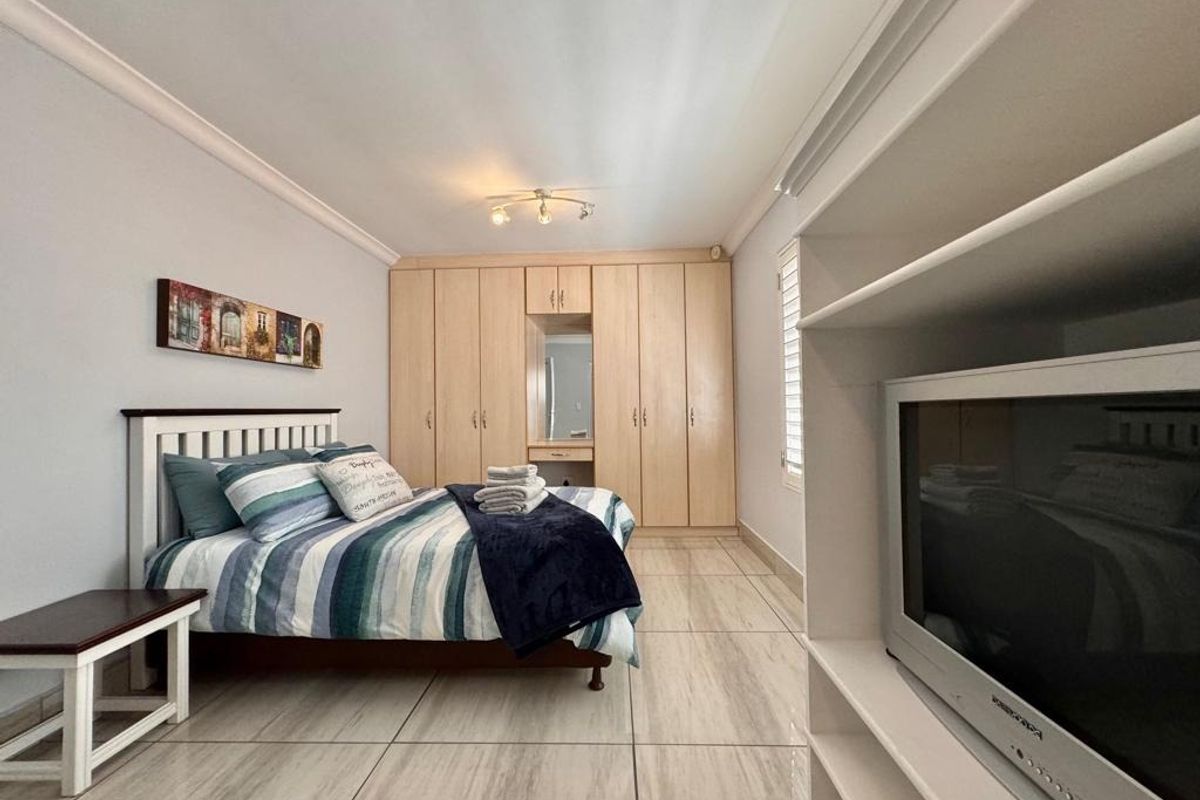 Spacious bedroom featuring extensive built-in cupboards, tiled flooring, and integrated shelving, offering a functional and well-maintained living space.
