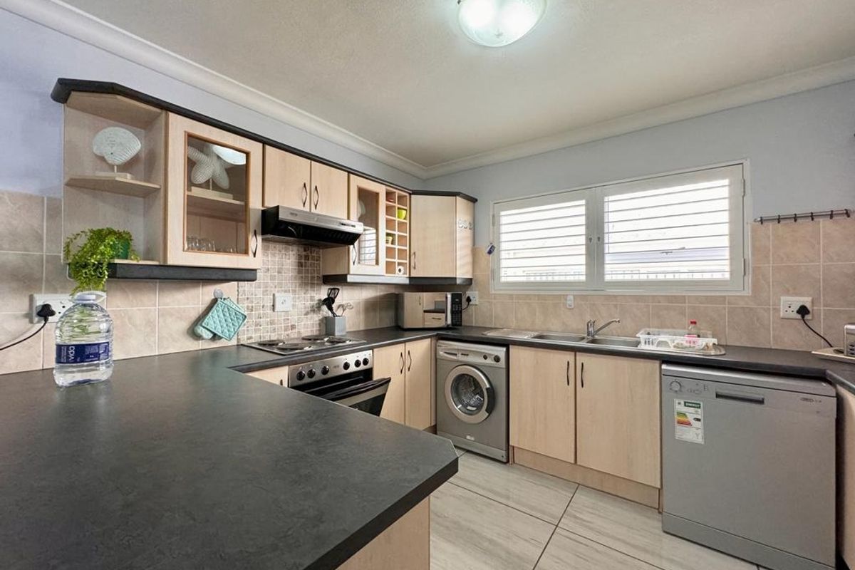 Functional kitchen featuring light wood cabinetry, dark laminate countertops, tiled backsplash, and integrated appliances including an oven, hob, and extractor fan.