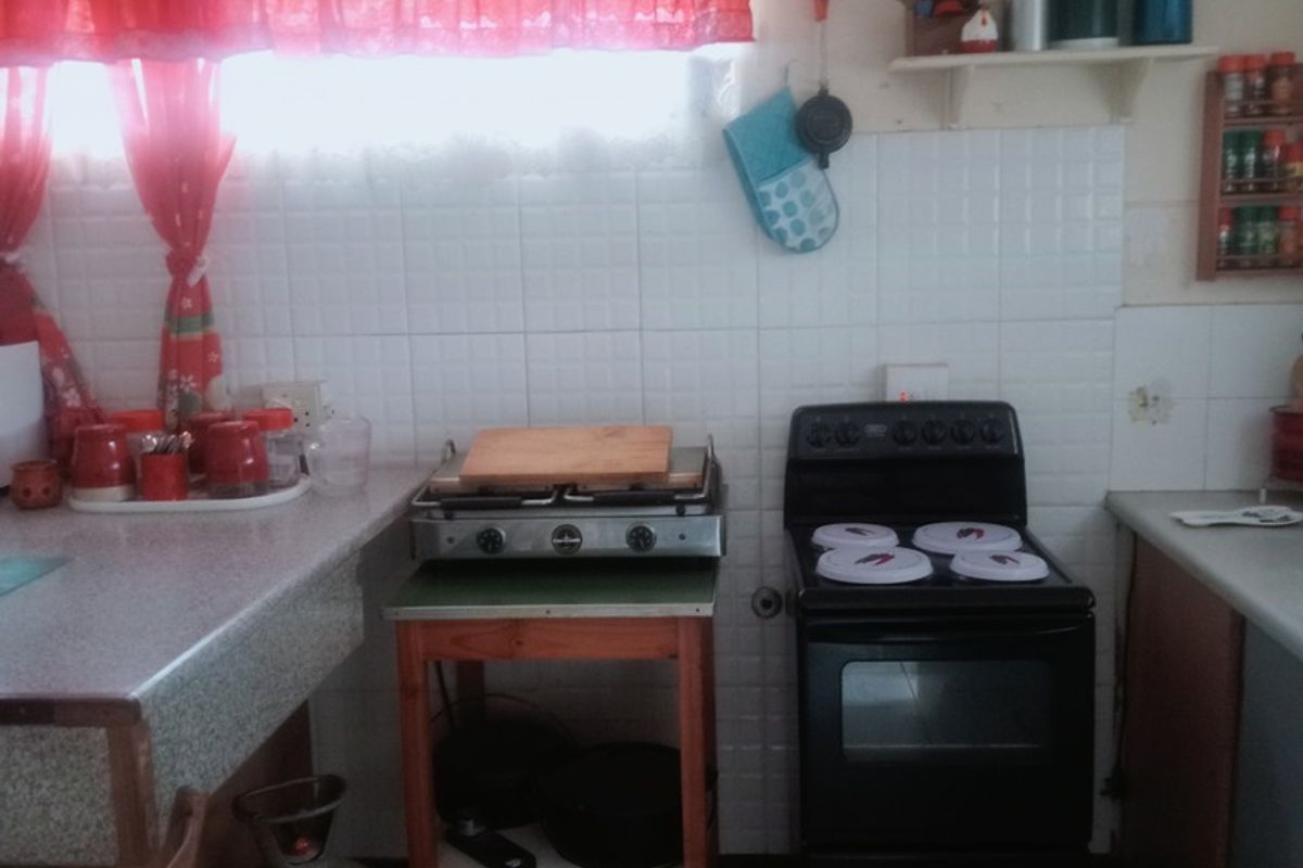 A functional kitchen area featuring a freestanding oven, gas hob, tiled splashback, and laminate countertops with tiled flooring.