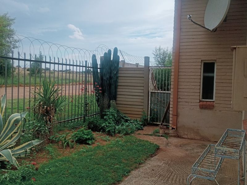 Rear exterior view of the property featuring a concrete patio area, brick wall, satellite dish, and perimeter security fencing with razor wire.