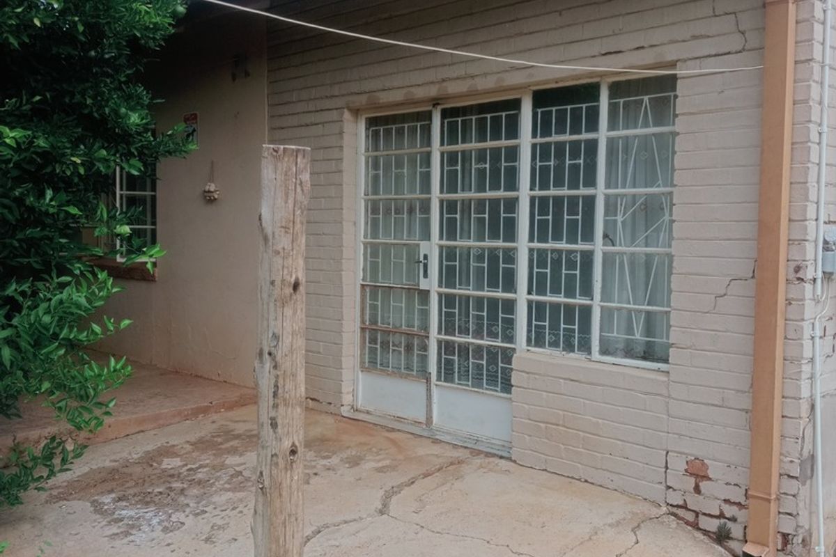 Rear exterior view of the house featuring a concrete patio, brick facade with visible cracks, and a sliding glass door with security bars.