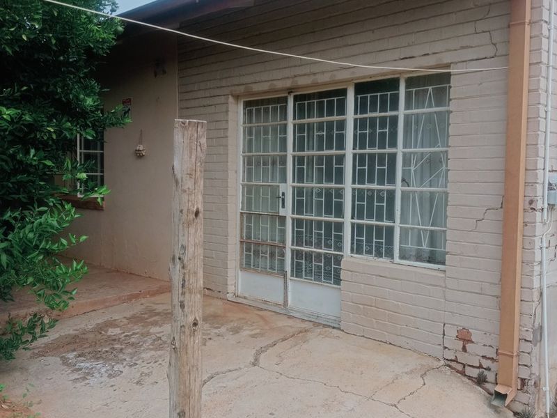 Rear exterior view of the house featuring a concrete patio, brick facade with visible cracks, and a sliding glass door with security bars.