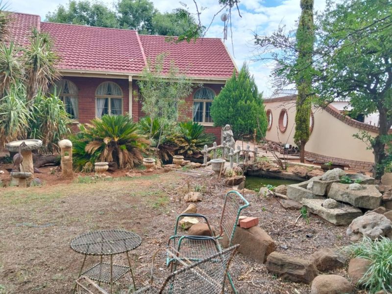 Rear garden area featuring a brick farmhouse facade, arched windows, a small stone bridge, and a garden pond.